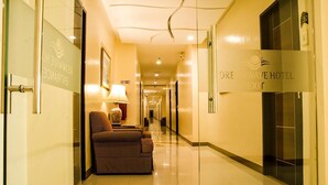 Un pasillo de hotel con un sofá de cuadros, una lámpara y un letrero que indica la salida.