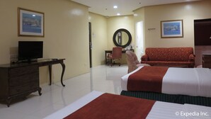 Habitación de hotel con una cama, un escritorio con televisor, un sofá rojo, un espejo y dos cuadros en la pared.