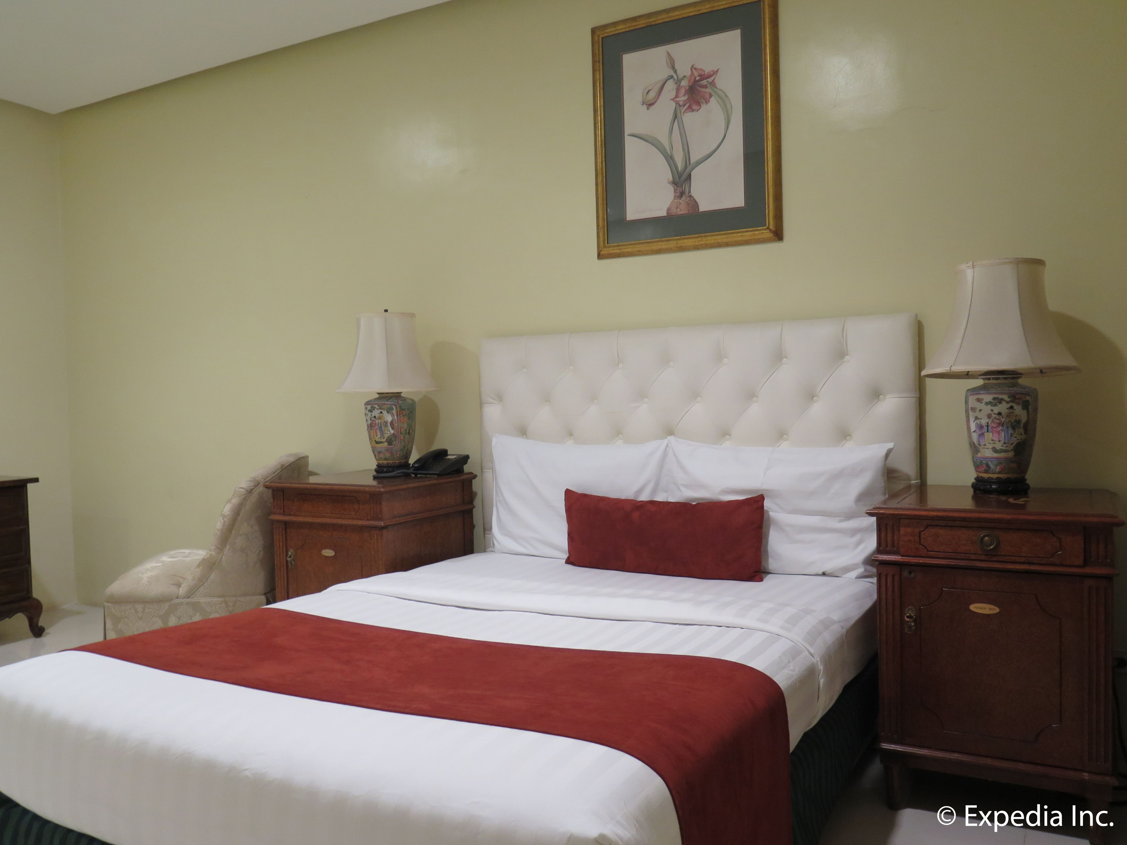 Habitación de hotel con una cama grande, dos mesitas de noche con lámparas, un teléfono y un cuadro en la pared.