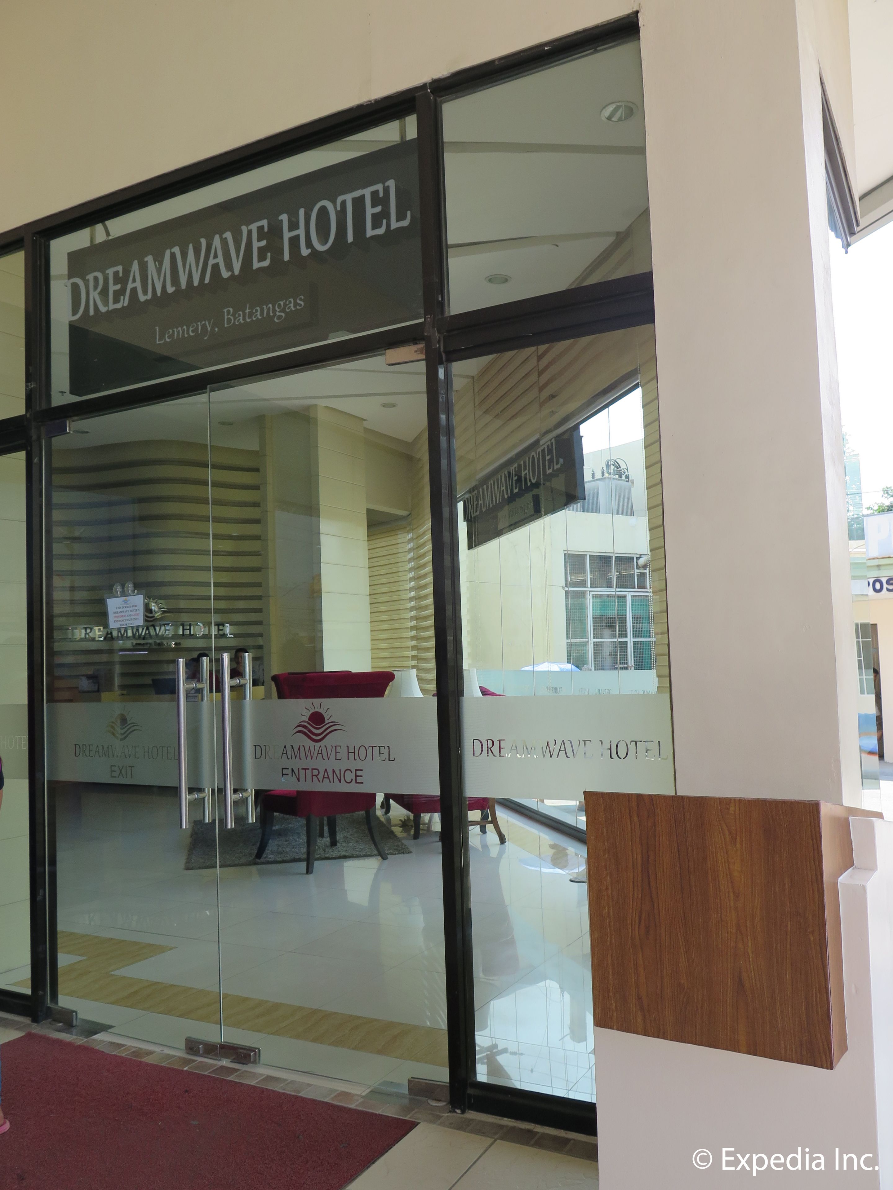 A entrada do Hotel Dreamwave, com sinalização clara, um balcão de recepção e um tapete vermelho que conduz ao interior.