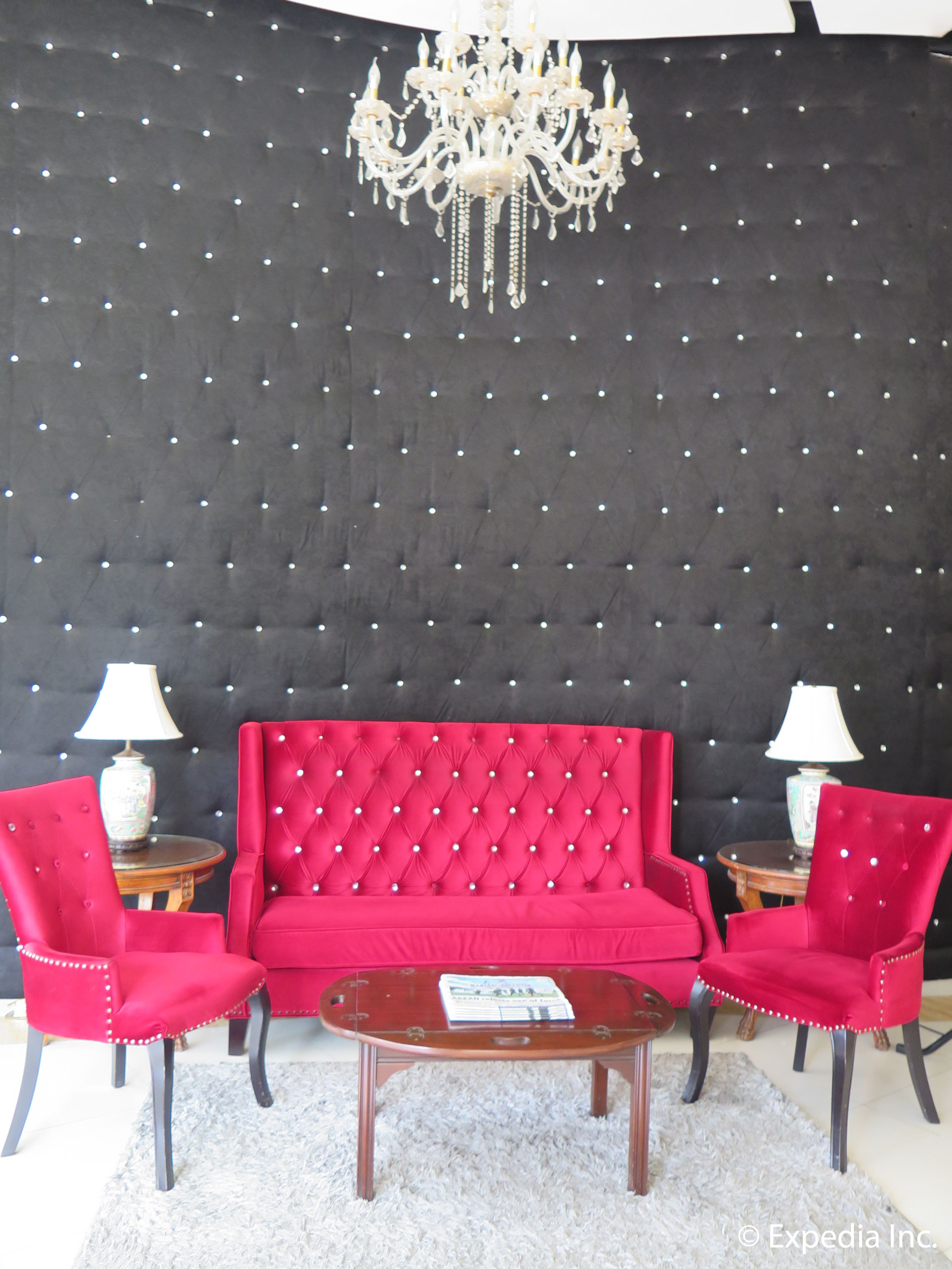 Um quarto com um sofá vermelho com capitonê, duas poltronas combinando, uma mesa de centro de madeira e um candelabro.