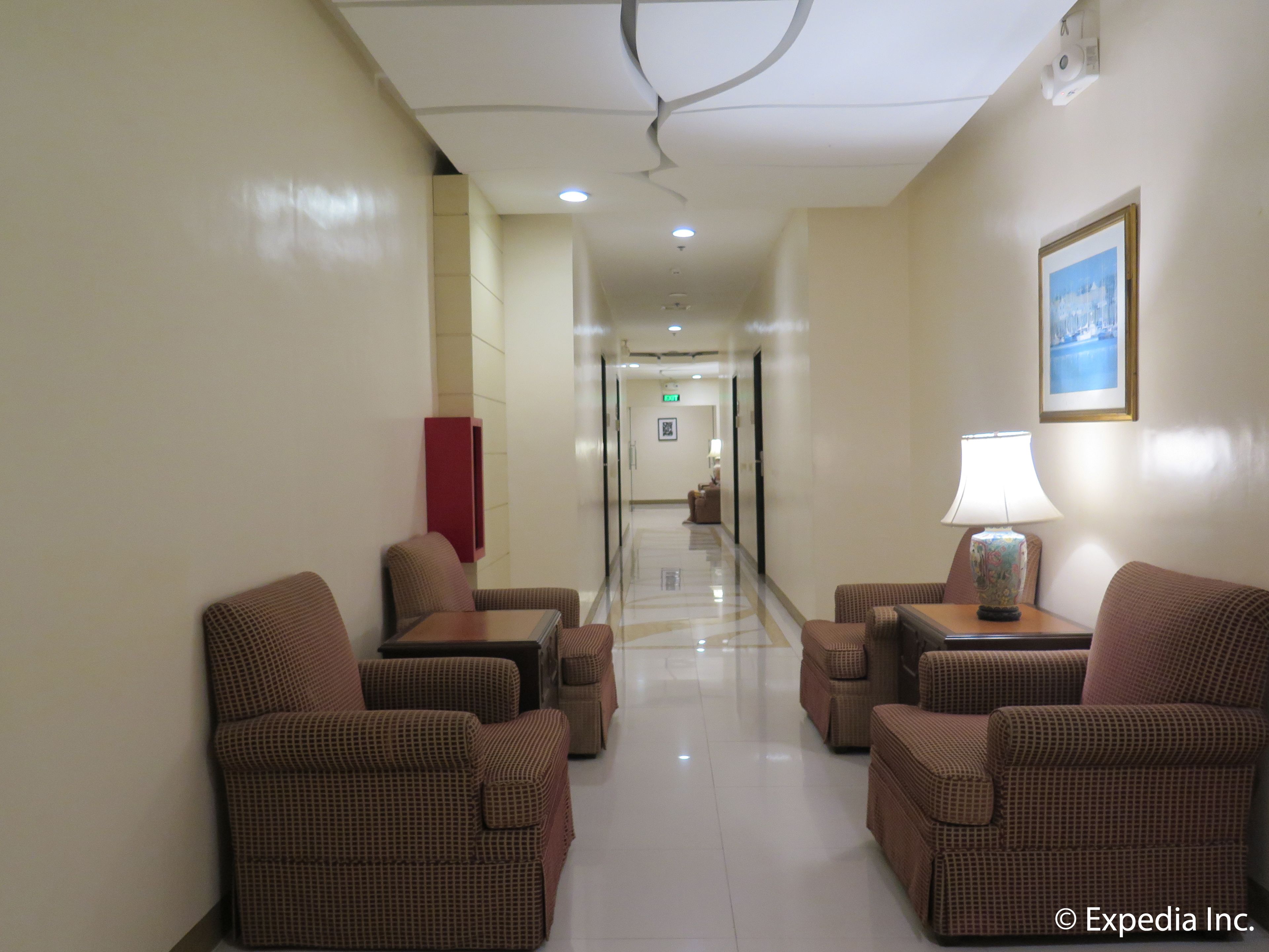 A hotel lobby with a long corridor, wicker furniture, a lamp, and a framed picture on the wall.