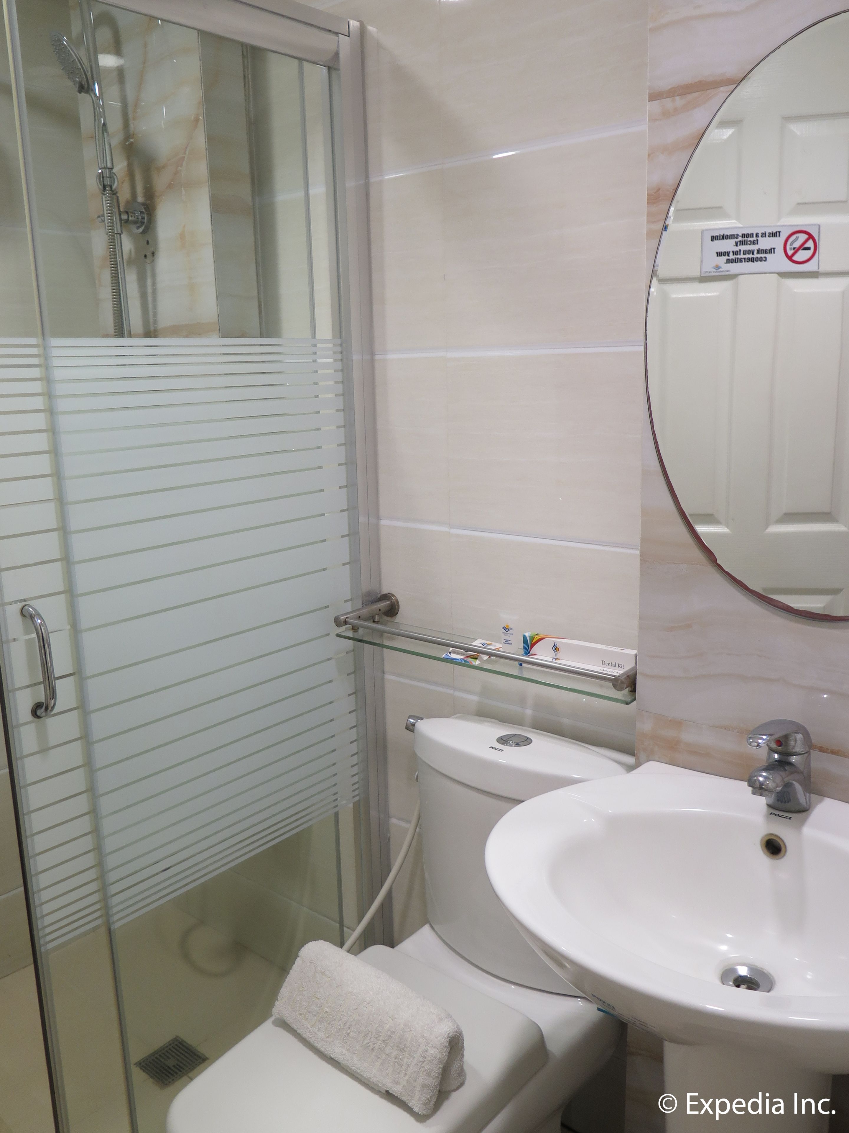 A bathroom with a glass shower enclosure, a toilet, a sink with a mirror, and a glass shelf with toiletries.