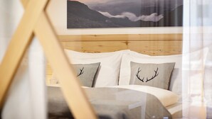 A bedroom with a wooden headboard, a bed with white bedding, and a mountain landscape painting above the bed. - Residence Settsass (Corvara in Badia)