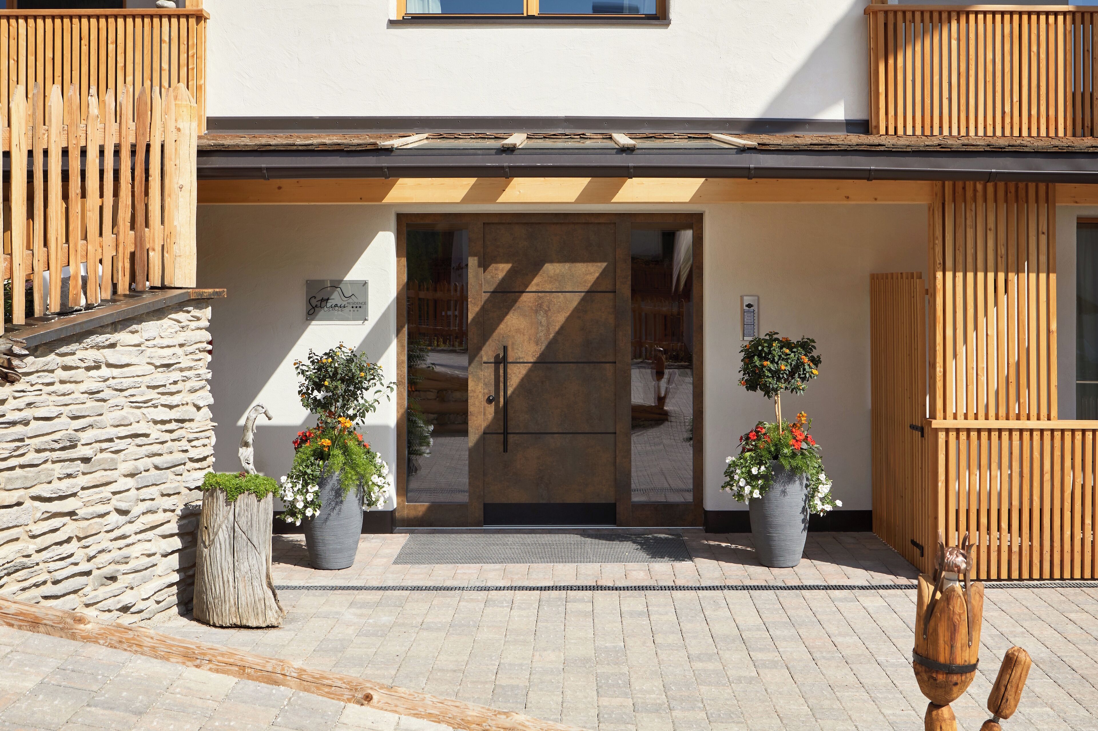 Une entrée d’immeuble avec une porte en bois, un mur en pierre et des plantes en pot.