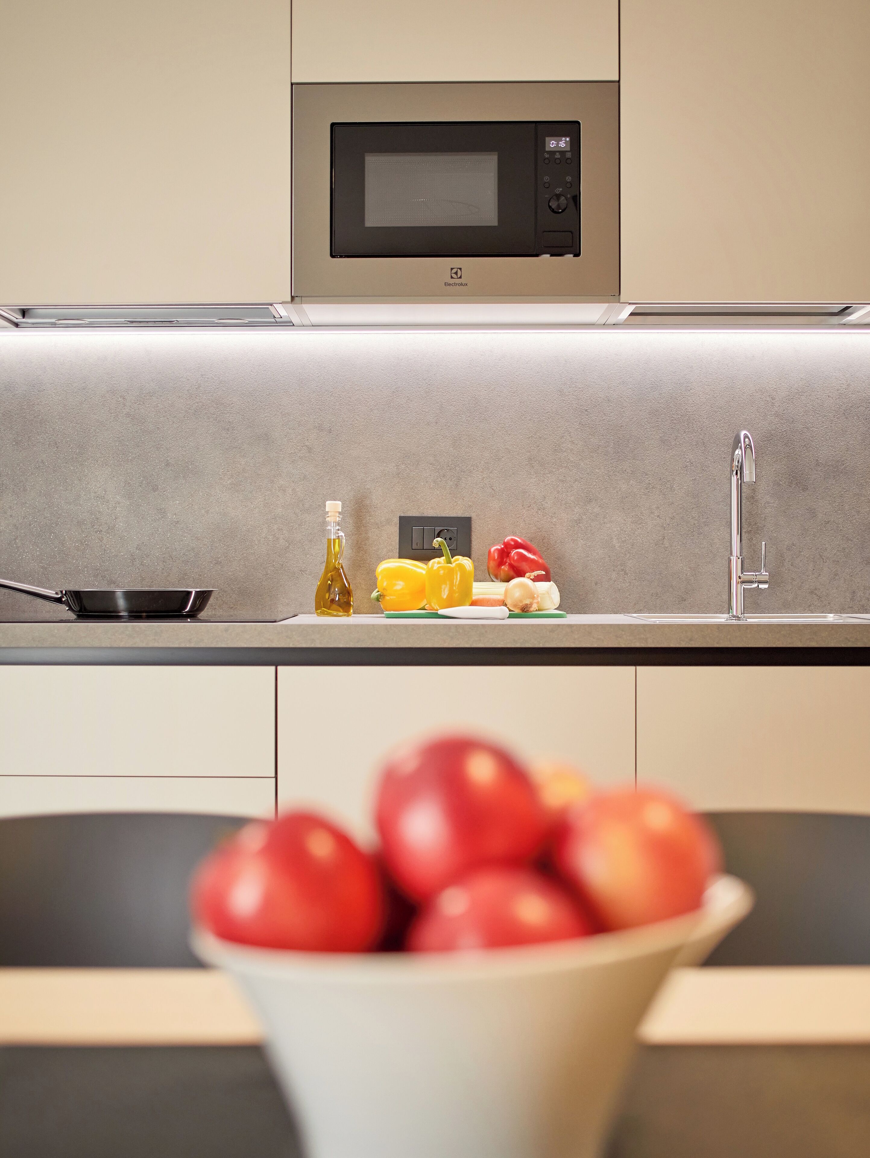 A modern kitchen with a built-in microwave, a sink, and a bowl of apples.