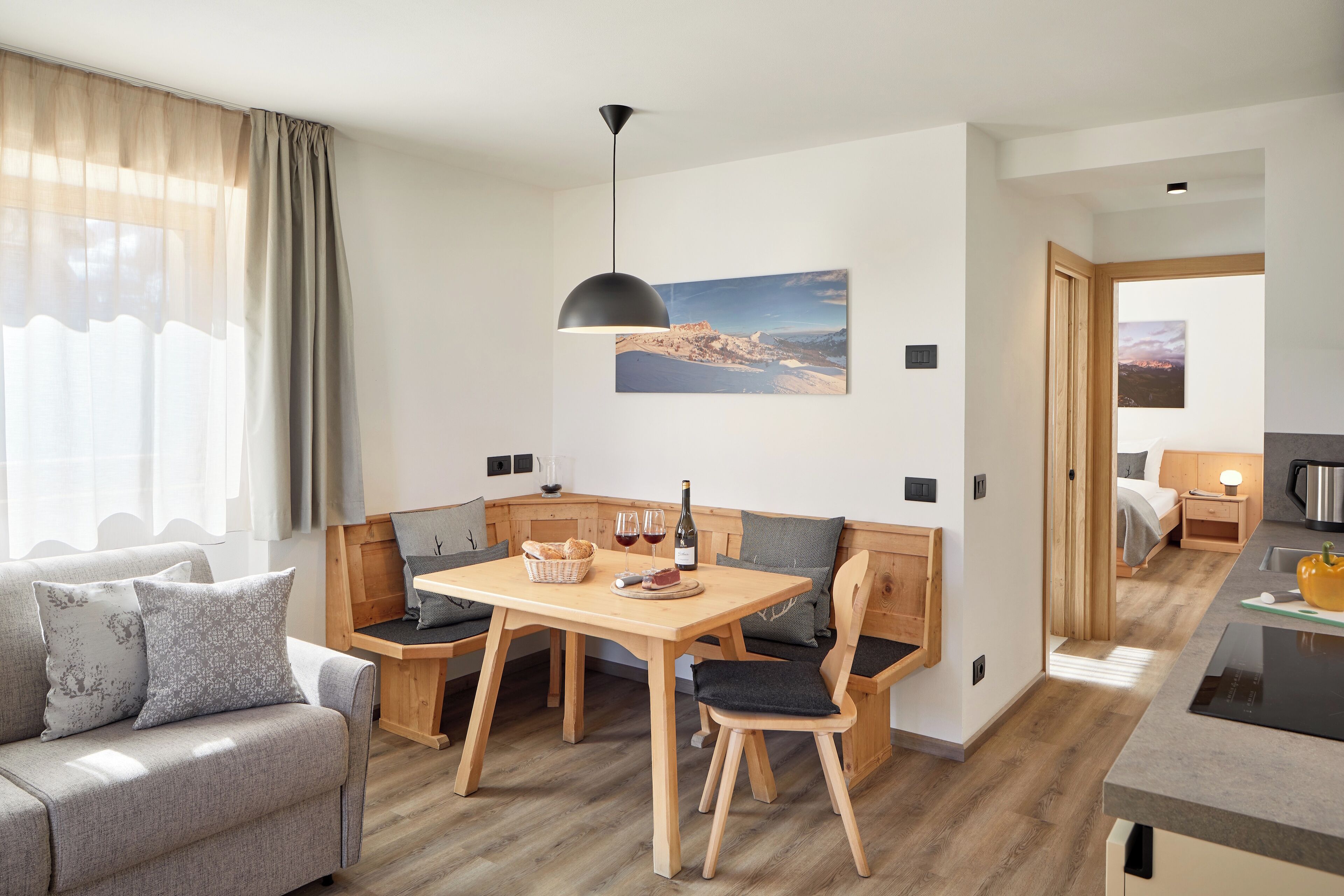 Une pièce moderne et bien éclairée, avec une table à manger en bois, des chaises et un canapé. Un tableau est accroché au mur, et la fenêtre offre une vue sur un paysage.