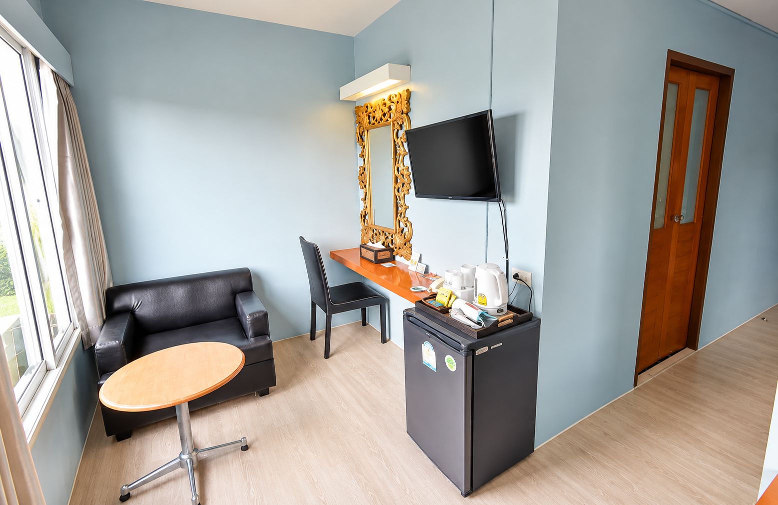 Habitación de hotel con sofá, escritorio, televisor de pantalla plana, refrigerador y ventana con cortinas.
