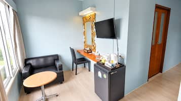 Habitación de hotel con sofá, escritorio, televisor de pantalla plana, refrigerador y ventana con cortinas.