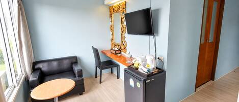 A hotel room with a sofa, a desk with a flat-screen TV, a refrigerator, and a window with curtains.