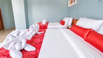 Habitación de hotel con dos camas, una con ropa de cama roja y blanca y la otra solo blanca. Hay toallas en el suelo y una mesita de noche de madera con una lámpara.
