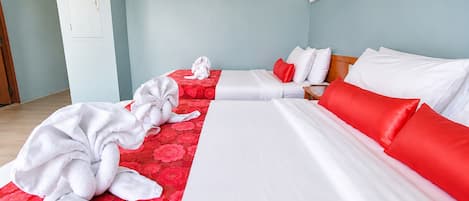 Habitación de hotel con dos camas, una con ropa de cama roja y blanca y la otra solo blanca. Hay toallas en el suelo y una mesita de noche de madera con una lámpara.