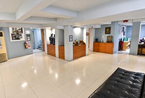 A hotel lobby with a reception desk, a black leather couch, and a fire extinguisher on the wall. - Villa Cha-Cha Khaosan-Rambuttri (Bangkok)