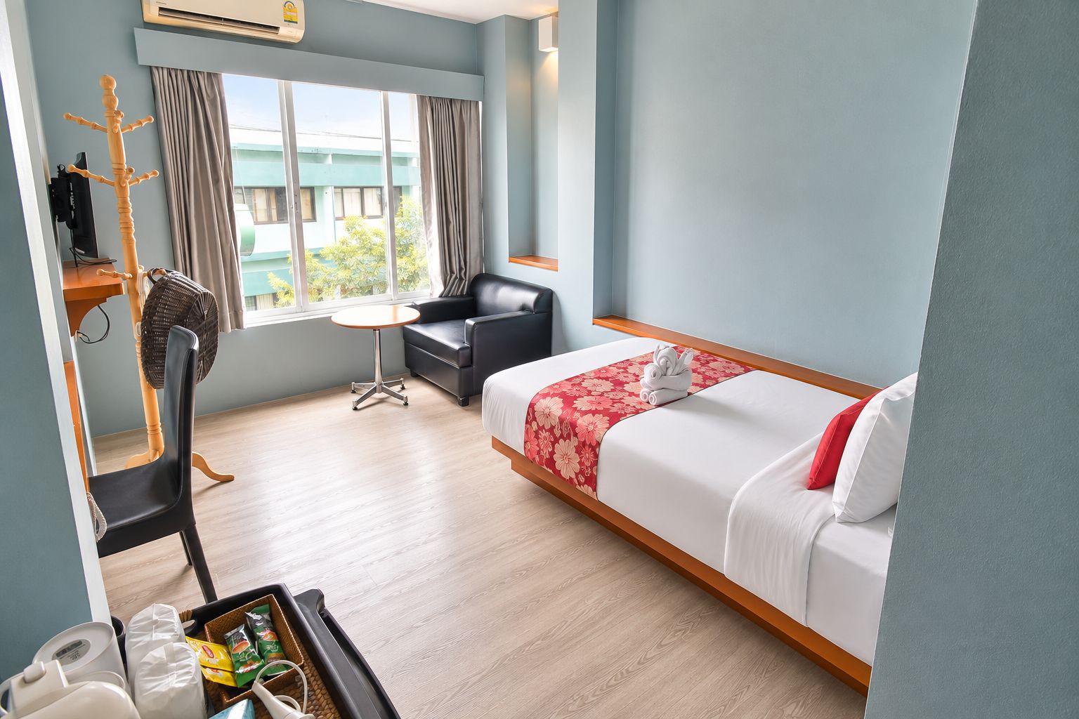 A hotel room with a bed, a desk, a chair, a fan, and a window with curtains.