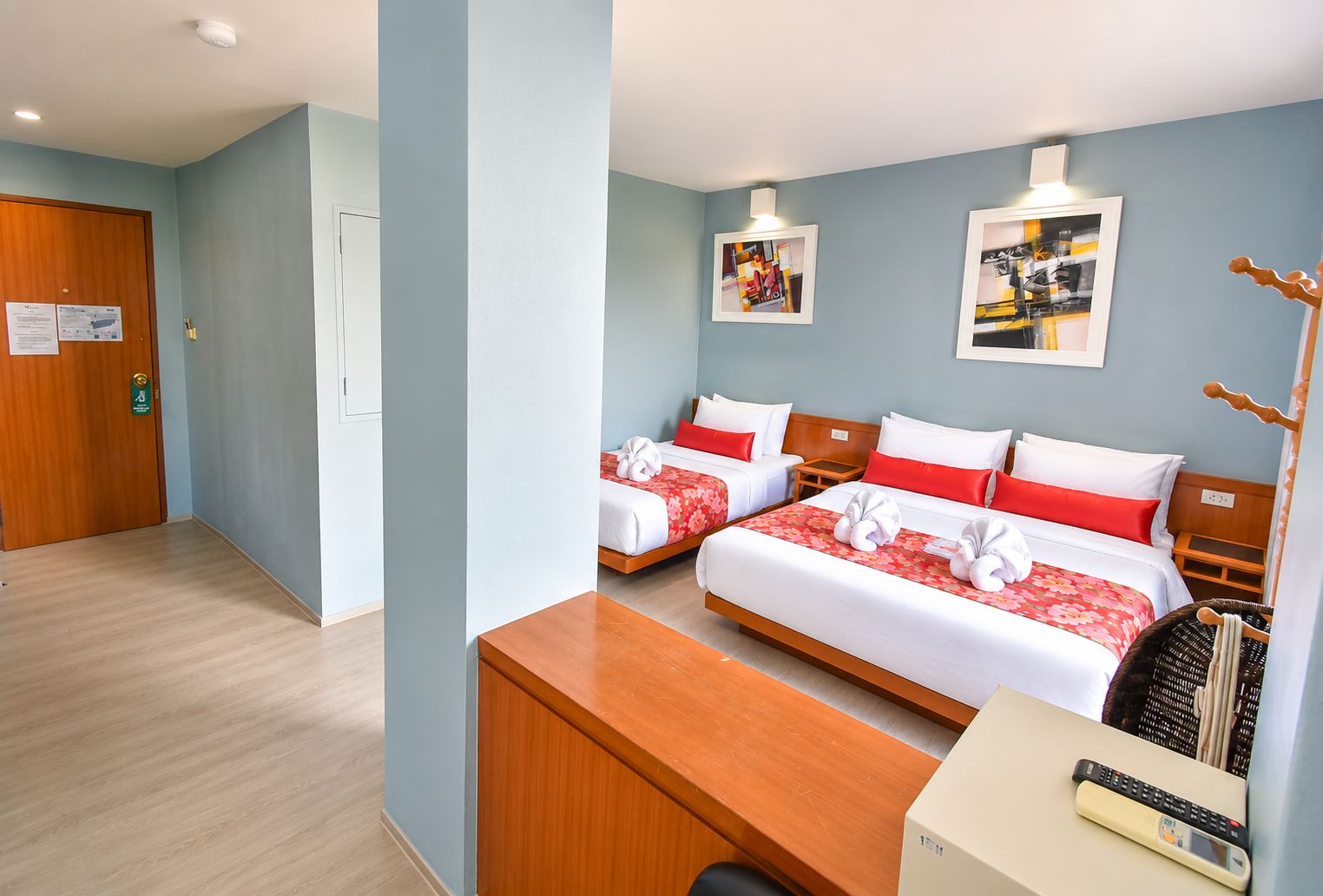 Een hotelkamer met twee bedden, een houten bureau, een stoel, een klein tafeltje en een televisie aan de muur.