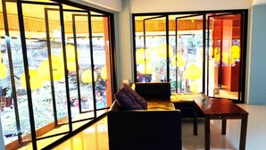 A modern living room with a sofa, a wooden table, and large windows with yellow lamps. - Villa Cha-Cha Khaosan-Rambuttri (Bangkok)