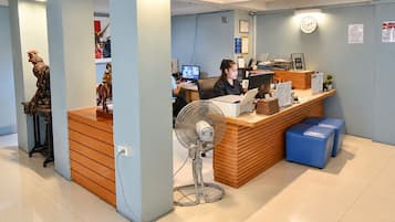 Zona de recepción con mostrador de madera, un escritorio con computadora, un ventilador y un reloj en la pared.