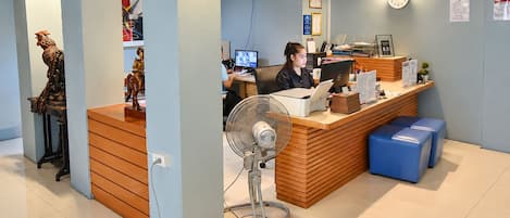 A reception area with a wooden counter, a desk with a computer, a fan, and a clock on the wall.