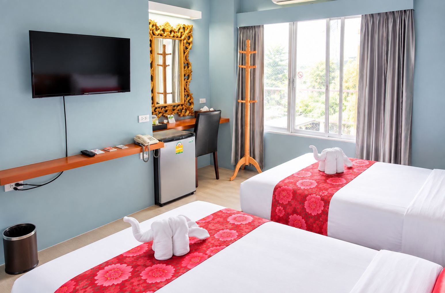 A hotel room with two beds, a desk, a television, a minibar, and a window with curtains.