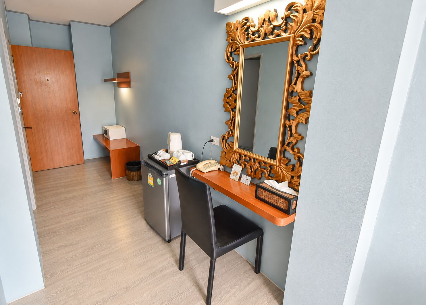 Una habitación de hotel con un escritorio, un espejo, un teléfono, una cafetera y un cesto de basura.
