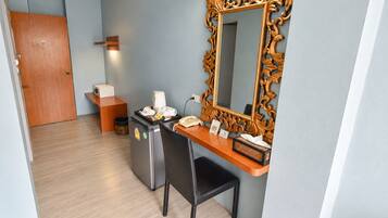 Una habitación de hotel con un escritorio, un espejo, un teléfono, una cafetera y un cesto de basura.