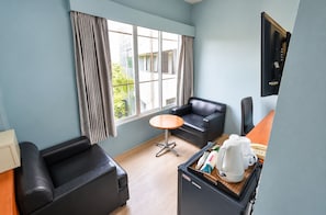 Ett hotellrum med en soffa, ett litet bord, ett kylskåp och ett fönster med gardiner.
