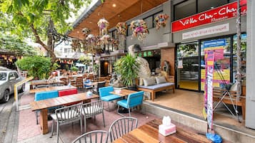 Un café al aire libre con mesas y sillas de madera, una estatua y decoraciones florales colgantes.