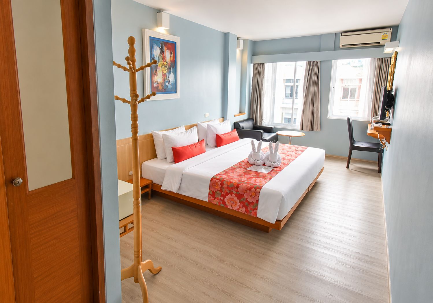 A hotel room with a bed, a desk, a chair, a window with curtains, and an air conditioning unit.