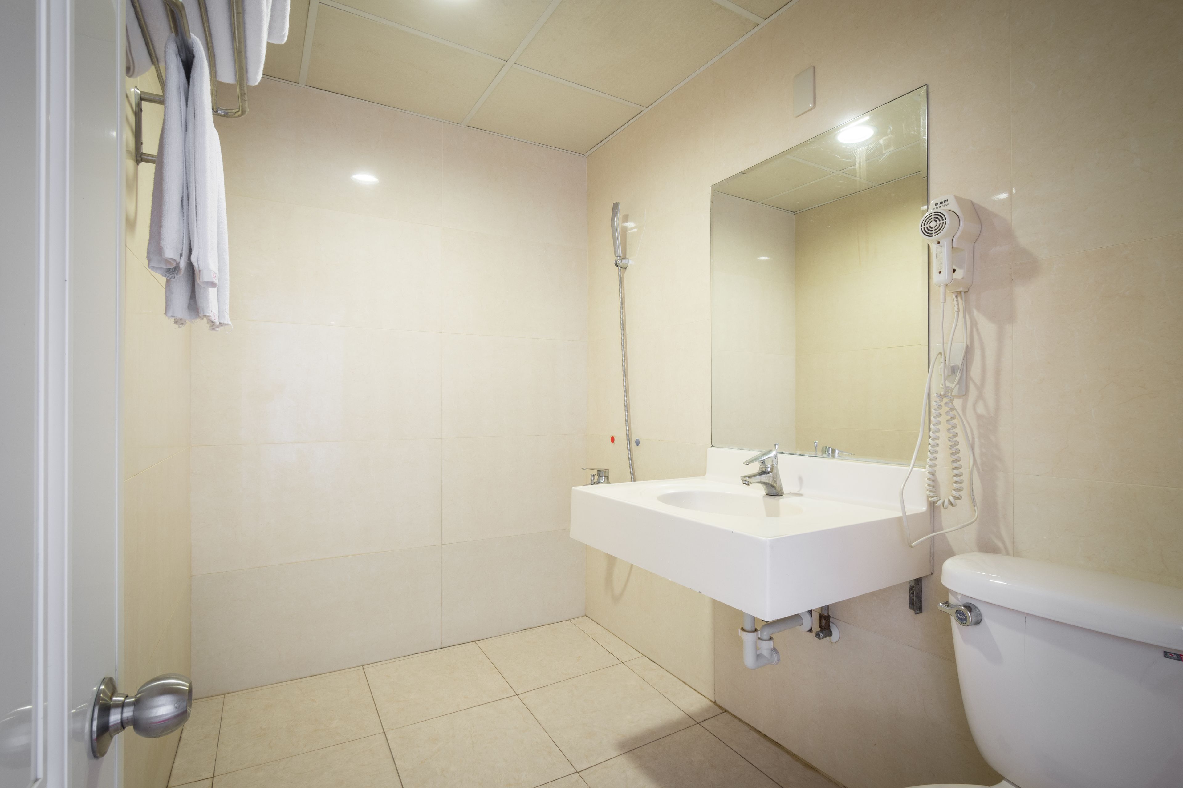 Um banheiro com pia branca, espelho e vaso sanitário. Toalhas penduradas em um suporte e um secador de cabelo na parede.