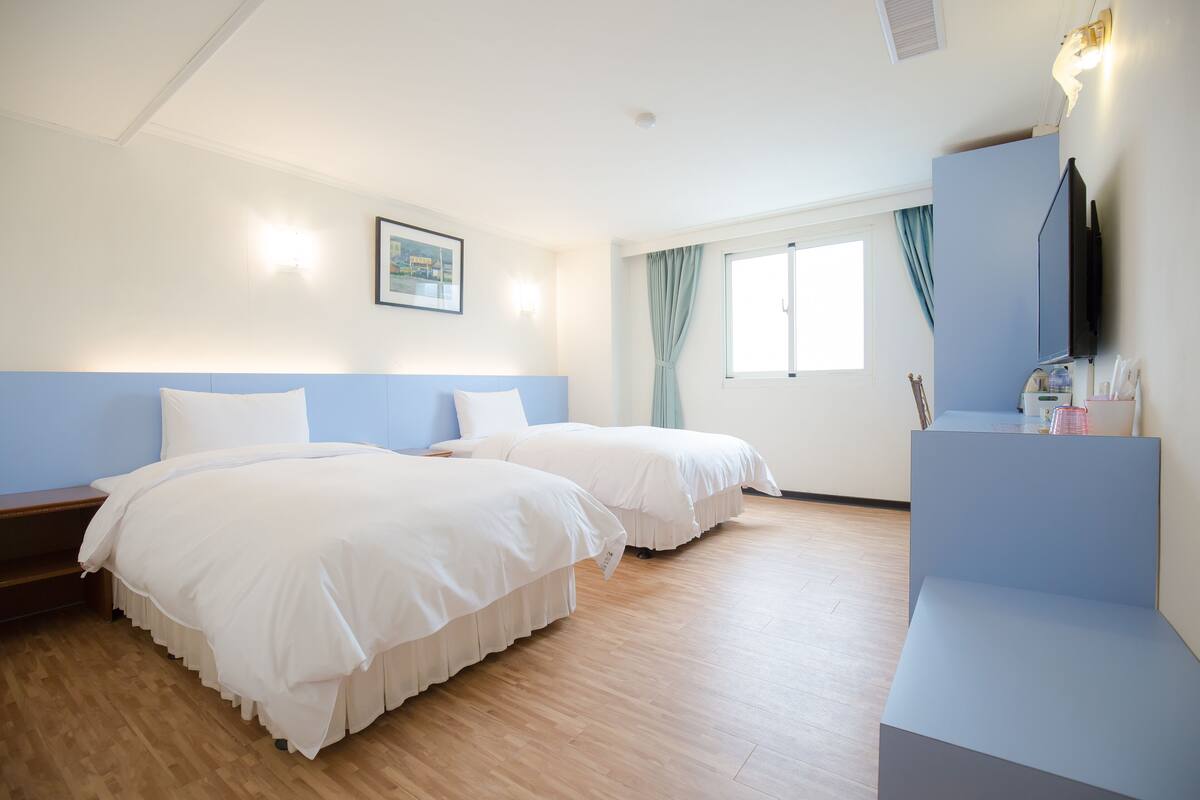 A hotel room with two beds, a desk, a television, and a window with curtains.