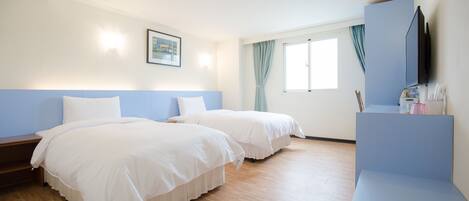 A hotel room with two beds, a desk, a television, and a window with curtains.