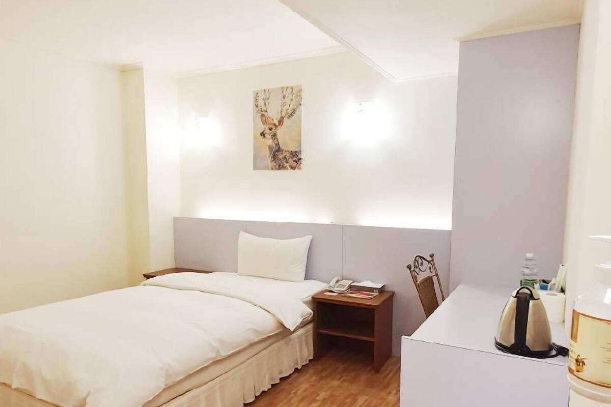 A bedroom with a bed, bedside table, nightstand, and a wall-mounted artwork.