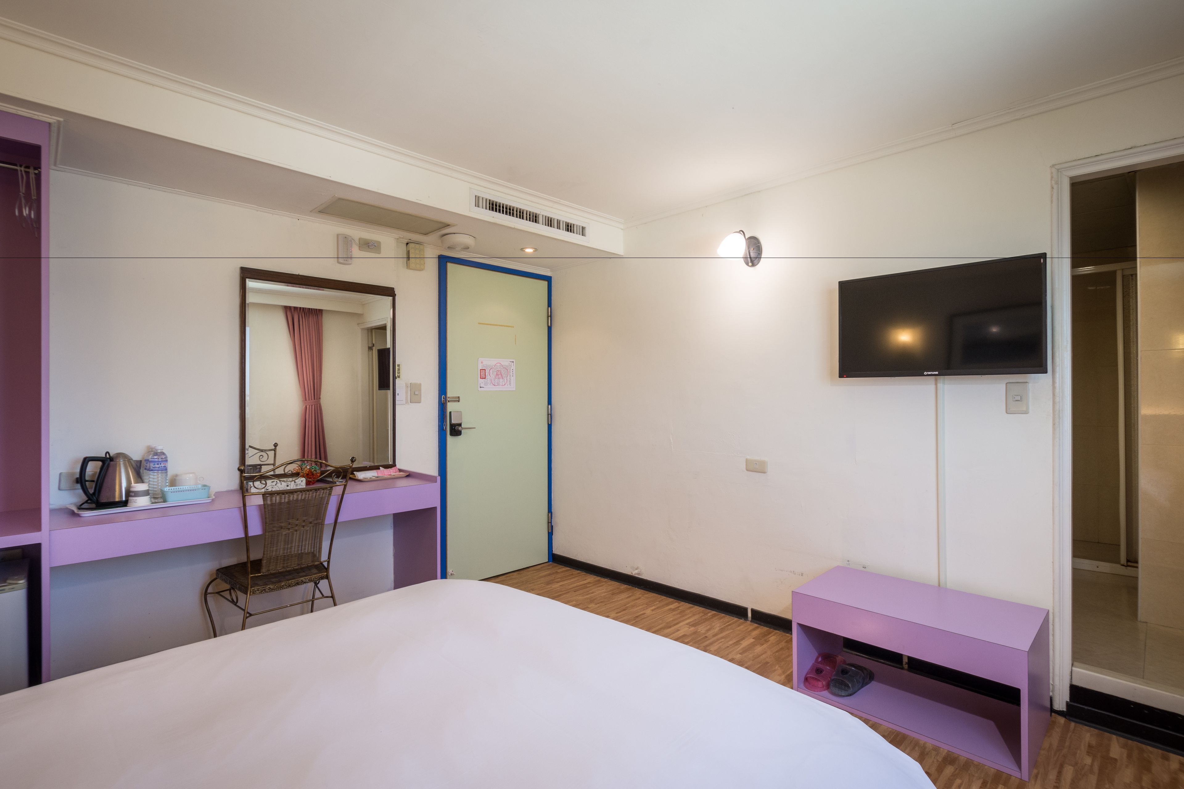 Een hotelkamer met een bed, een bureau met stoel, een televisie en een badkamers deur.