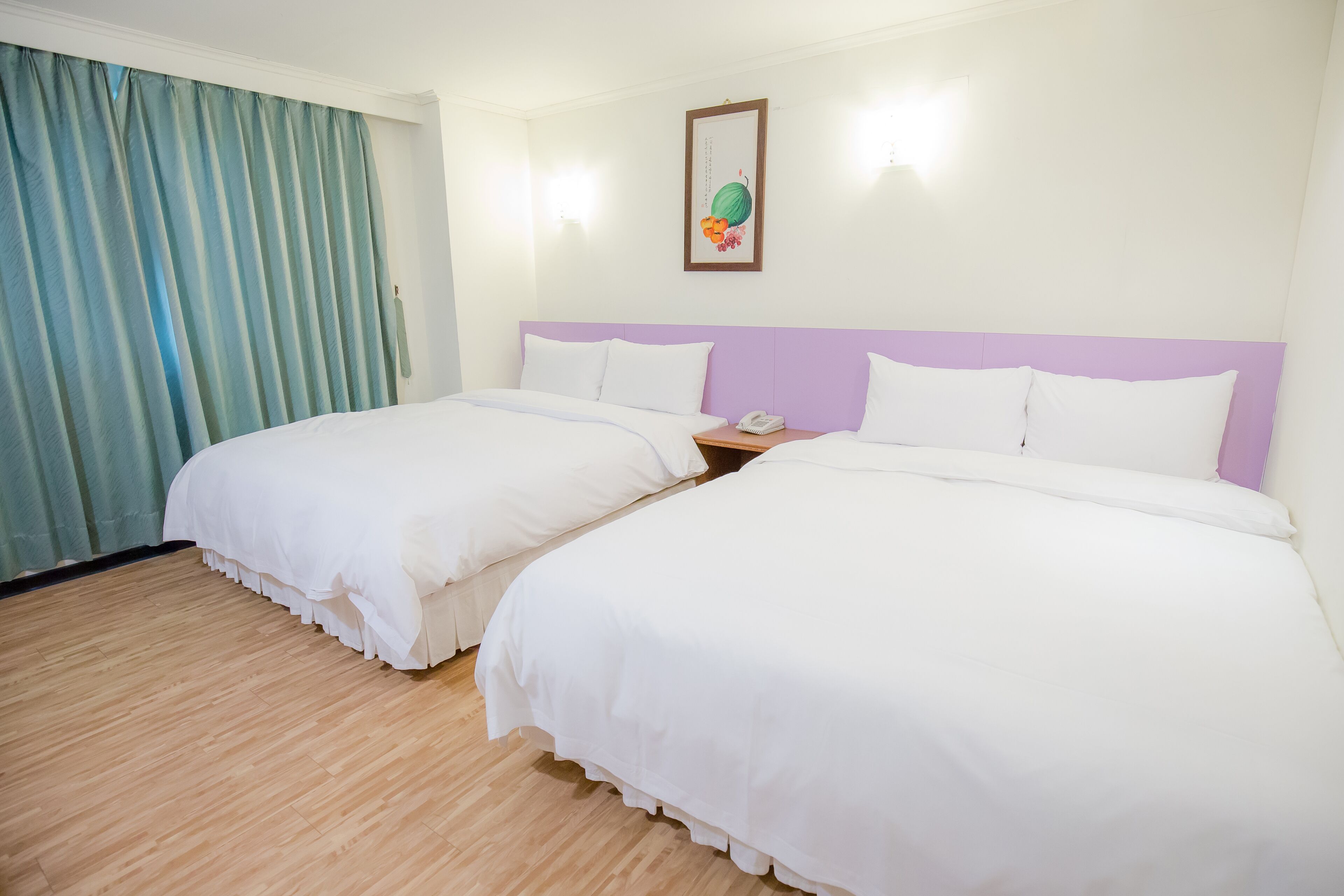 A hotel room with two beds, a wooden floor, a purple headboard, and a wall-mounted phone.