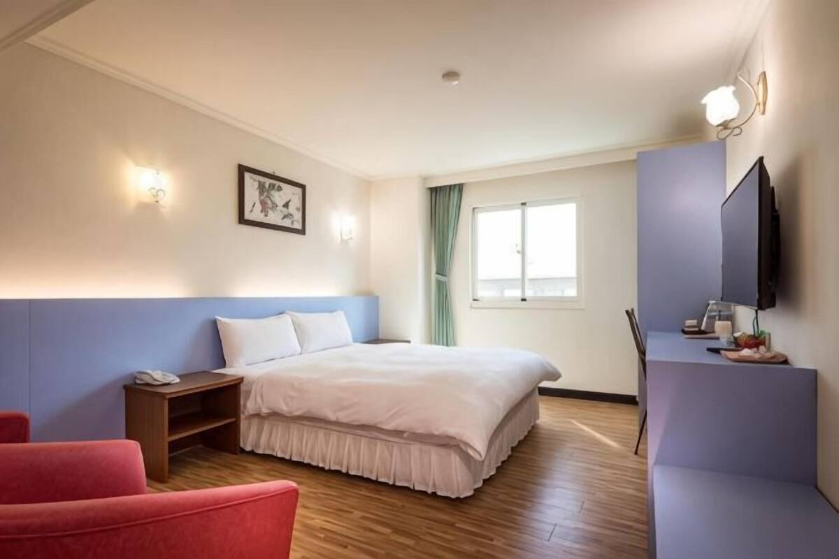 A hotel room with a bed, a desk, a chair, a TV, and a window with curtains.