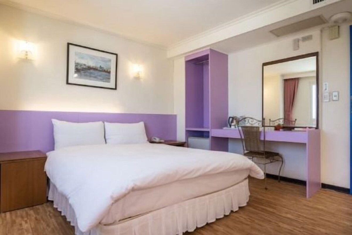 A bedroom with a bed, a nightstand, a desk, a chair, and a mirror.