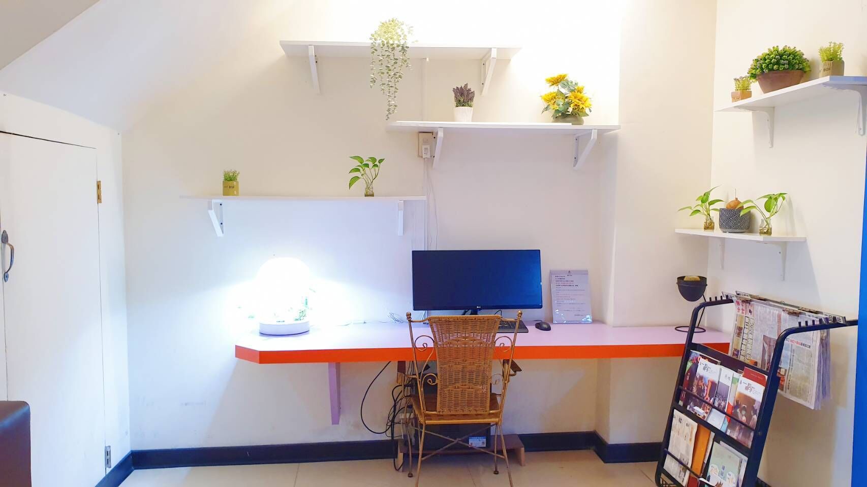 A small office with a desk, computer, chair, and shelves with plants.