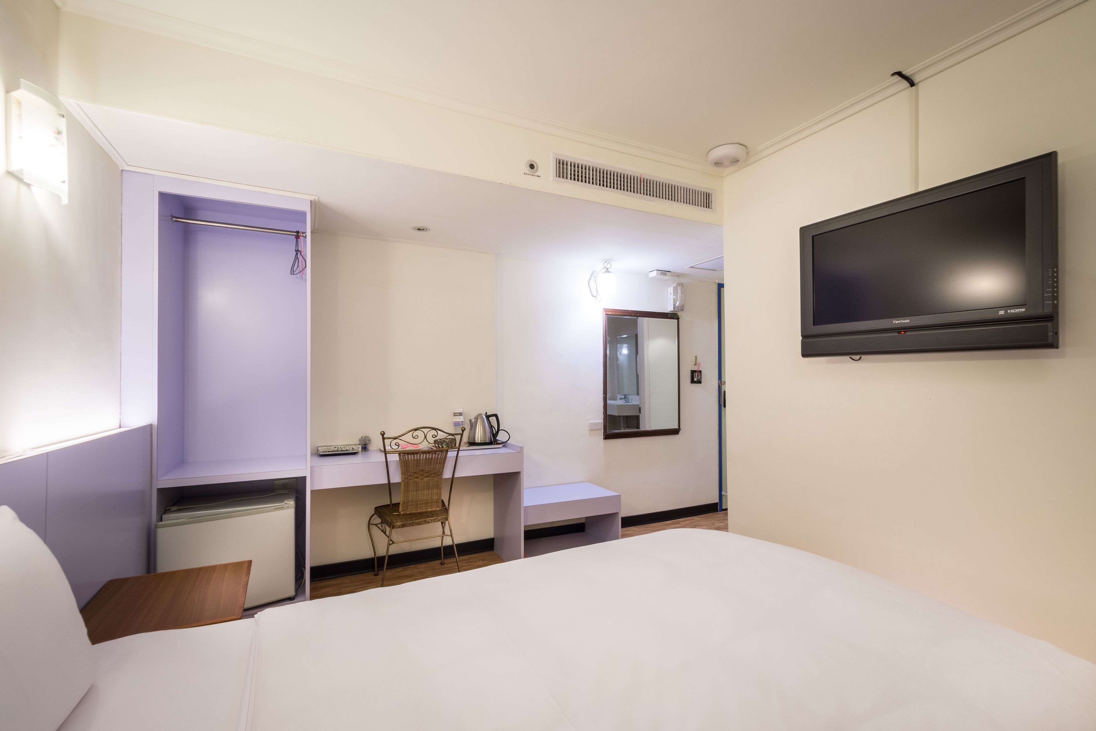 A hotel room with a bed, a desk with a chair, a television, and a wardrobe.