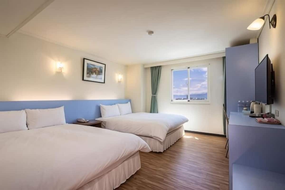 A hotel room with two beds, a desk, a TV, and a window with a view.