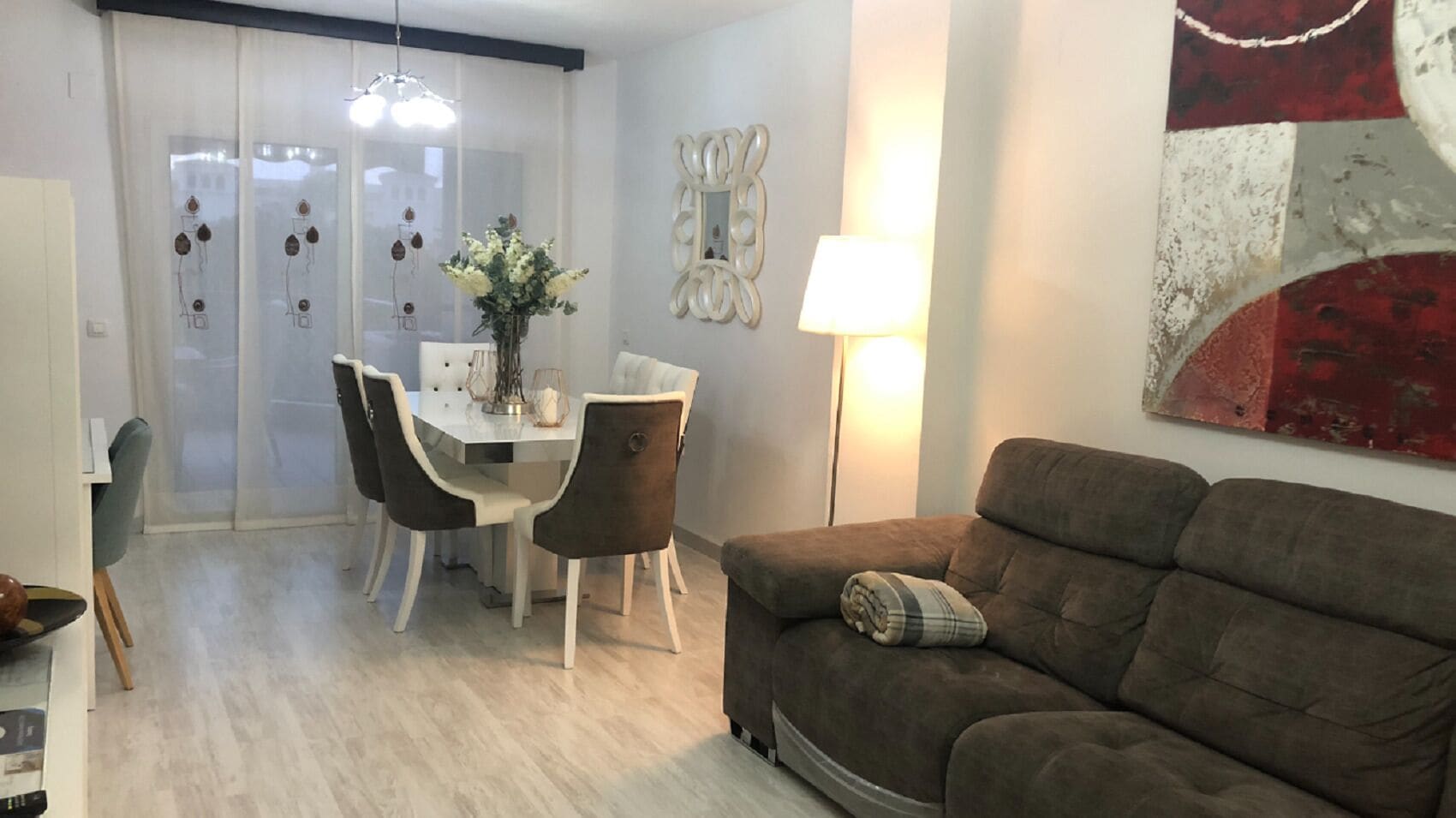 Un salon avec un canapé marron, une table à manger avec des chaises et un vase de fleurs.