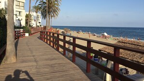 A wooden boardwalk leading to a beach with palm trees and a clear blue sky.