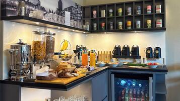 A modern breakfast bar with a coffee machine, fruit, and a beverage cooler.