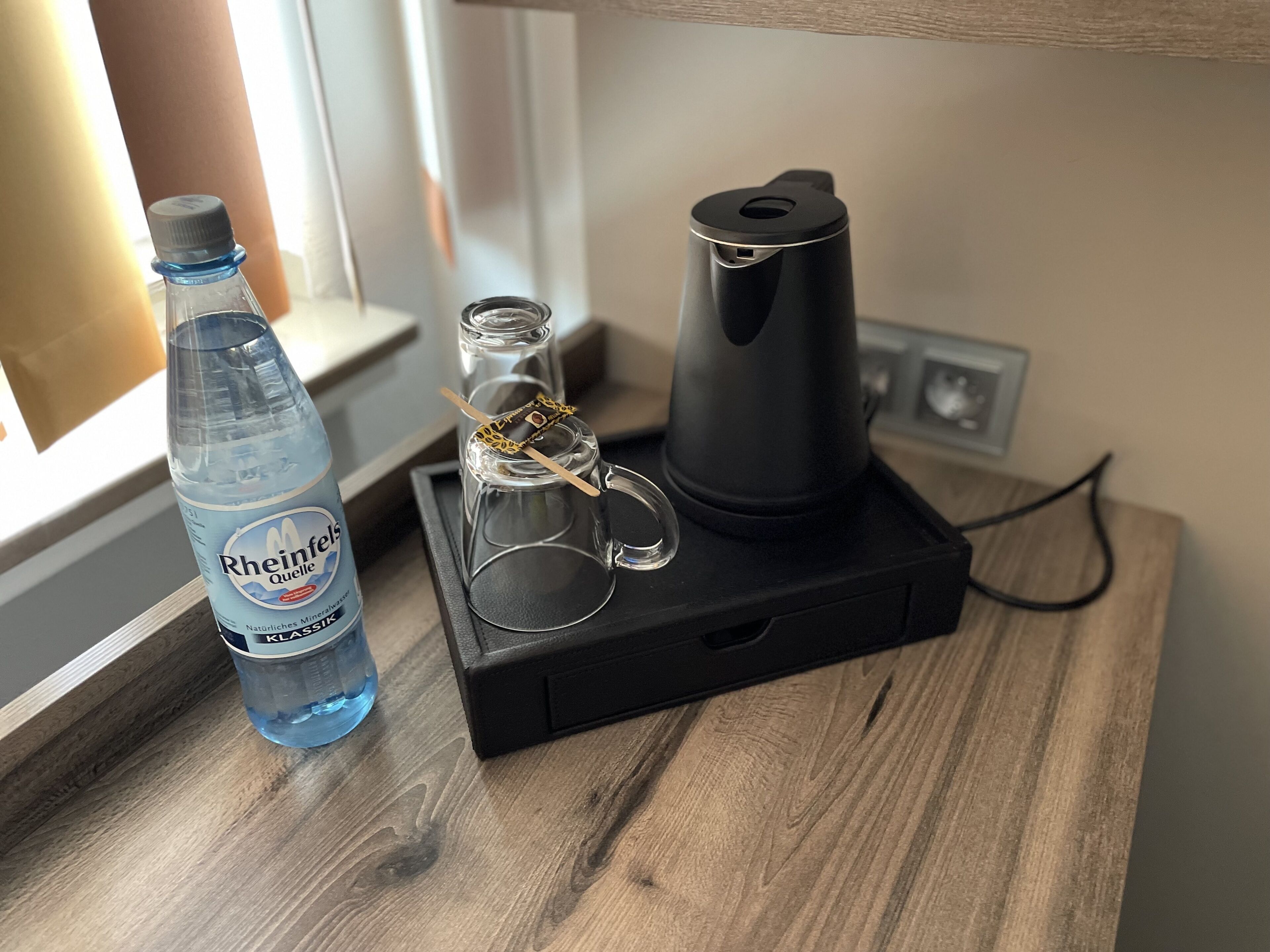 A bottle of water, a glass with a tea bag, and a coffee maker on a wooden surface.