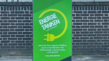 En grön reklamskylt för Stadtwerke Duisburg som marknadsför energibesparingar, med en symbol för ett eluttag och text.