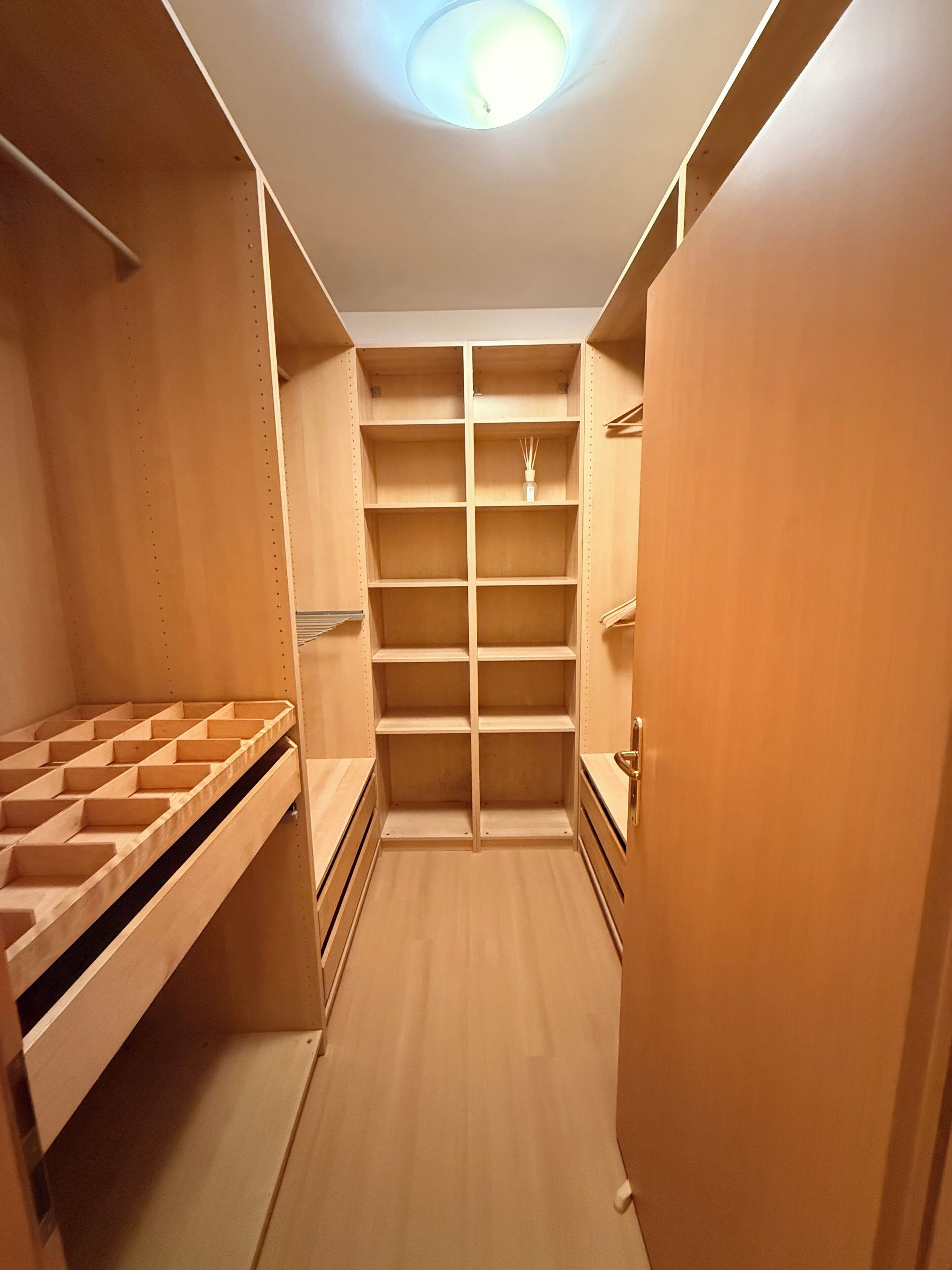 A walk-in closet with multiple shelves and drawers, a hanging rod, and a ceiling light.