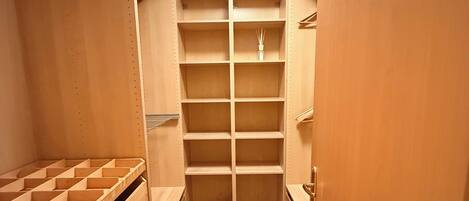 A walk-in closet with multiple shelves and drawers, a hanging rod, and a ceiling light.