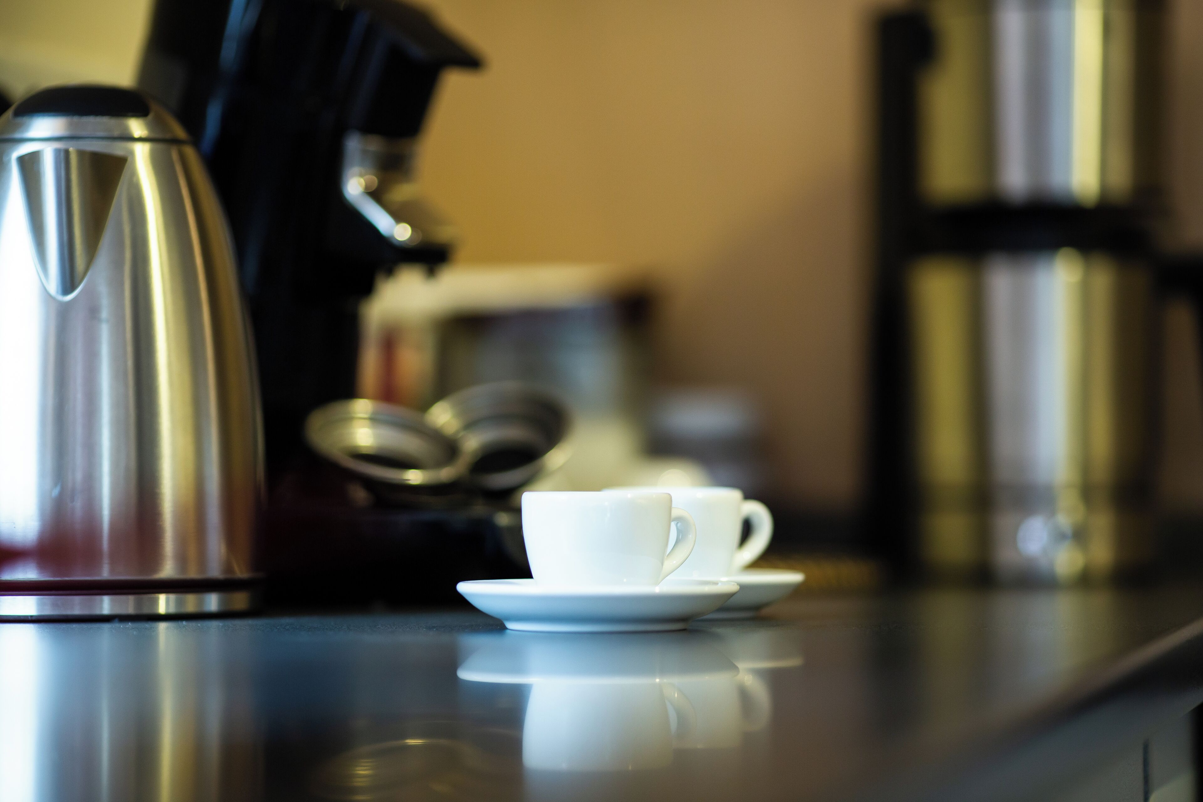 Una cafetera, una taza y un platillo sobre una superficie reflectante.