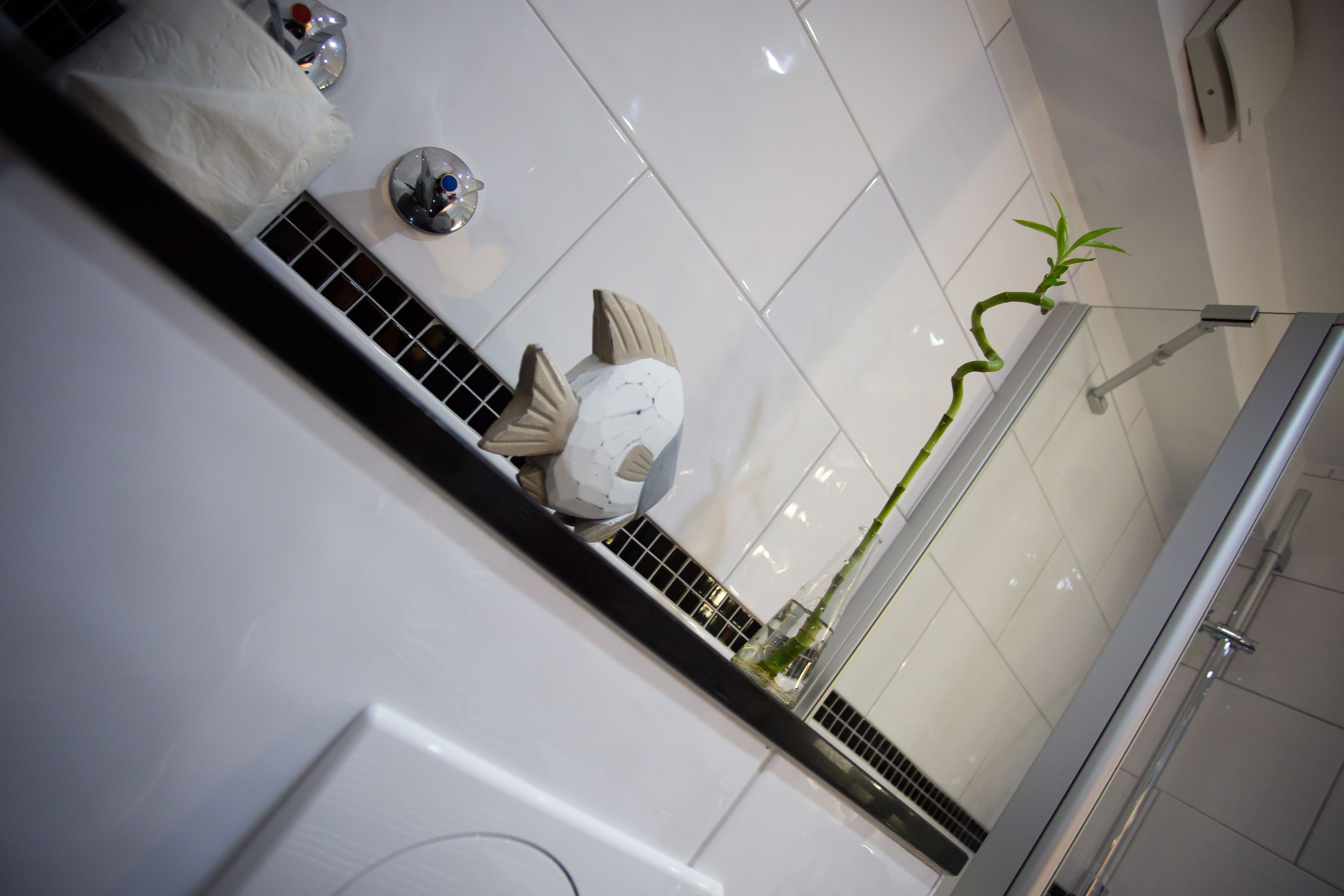 Un baño moderno con suelo de baldosas blancas, cabina de ducha con mampara de vidrio y una planta verde.