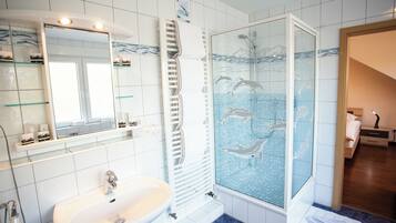 Een badkamer met een witte wastafel, een douchecabine met glazen wanden en een afbeelding van dolfijnen, en een betegelde vloer.