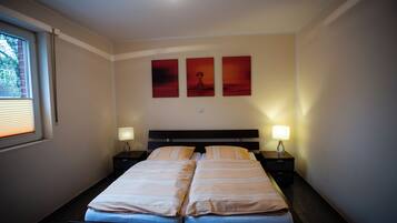 Una cama doble con dos mesitas de noche, cada una con una lámpara, en una habitación con una ventana y tres obras de arte colgadas en la pared.